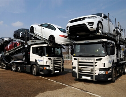 two Acumen Logistics car transporters parked next to each other with Range Rovers on one and Jaguars on the other.